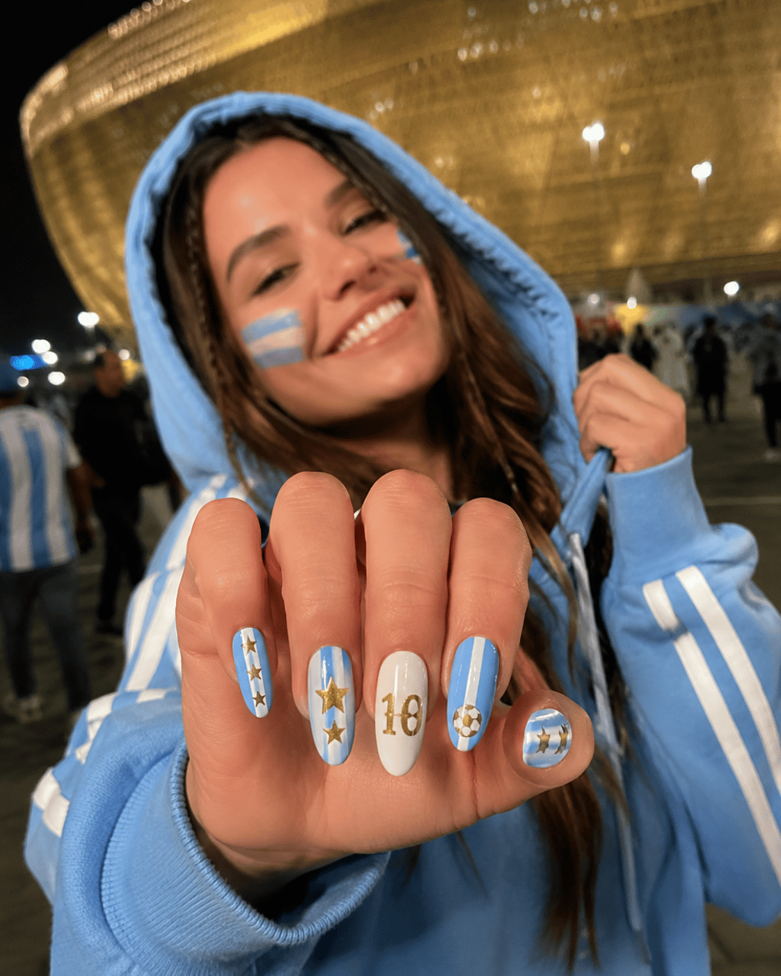 Argentina fan pride nails featuring sky blue and white football-inspired nail art with championship star accents outside a stadium.