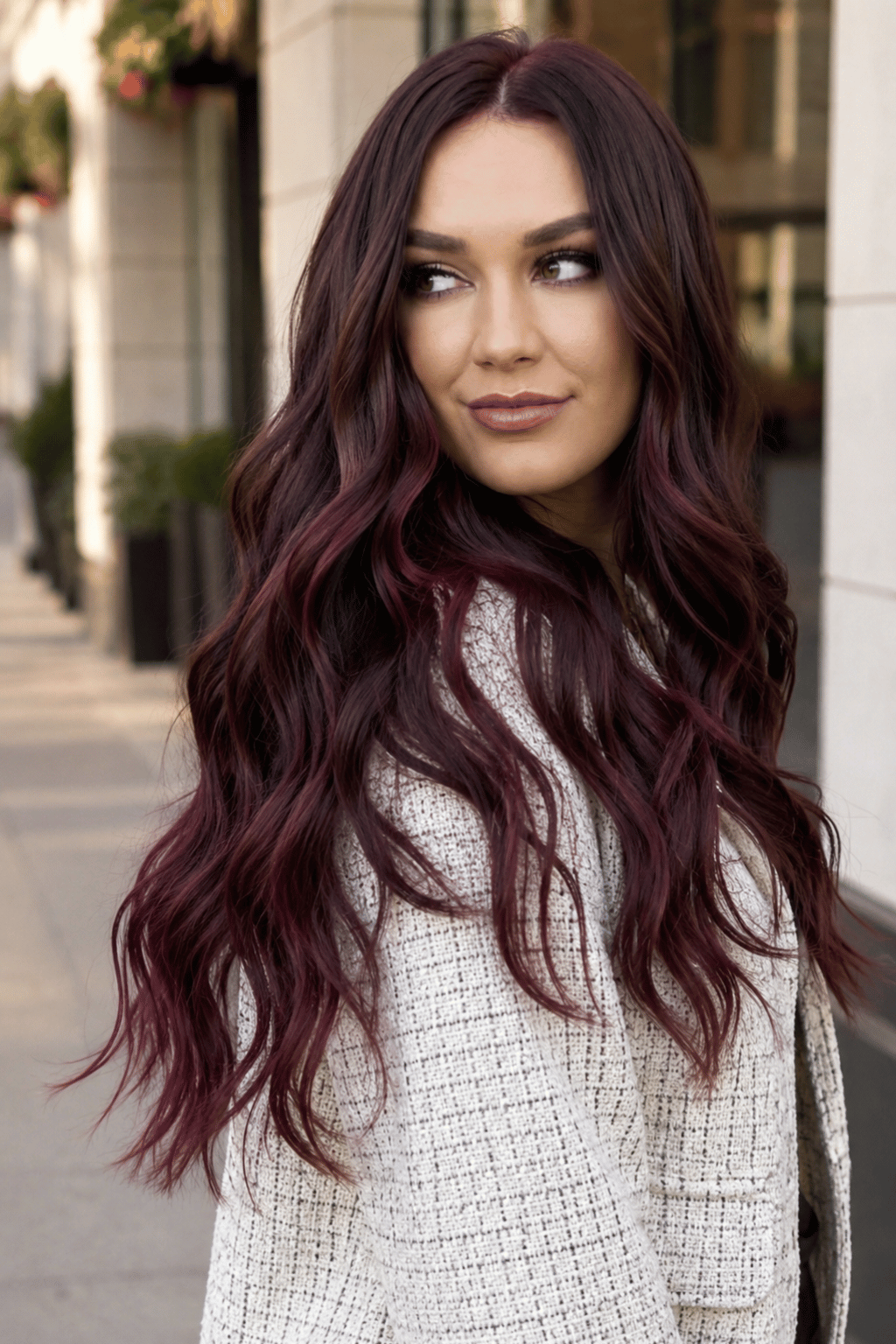 Woman with dark plum balayage on long wavy hair featuring deep brunette roots and dimensional plum ends.