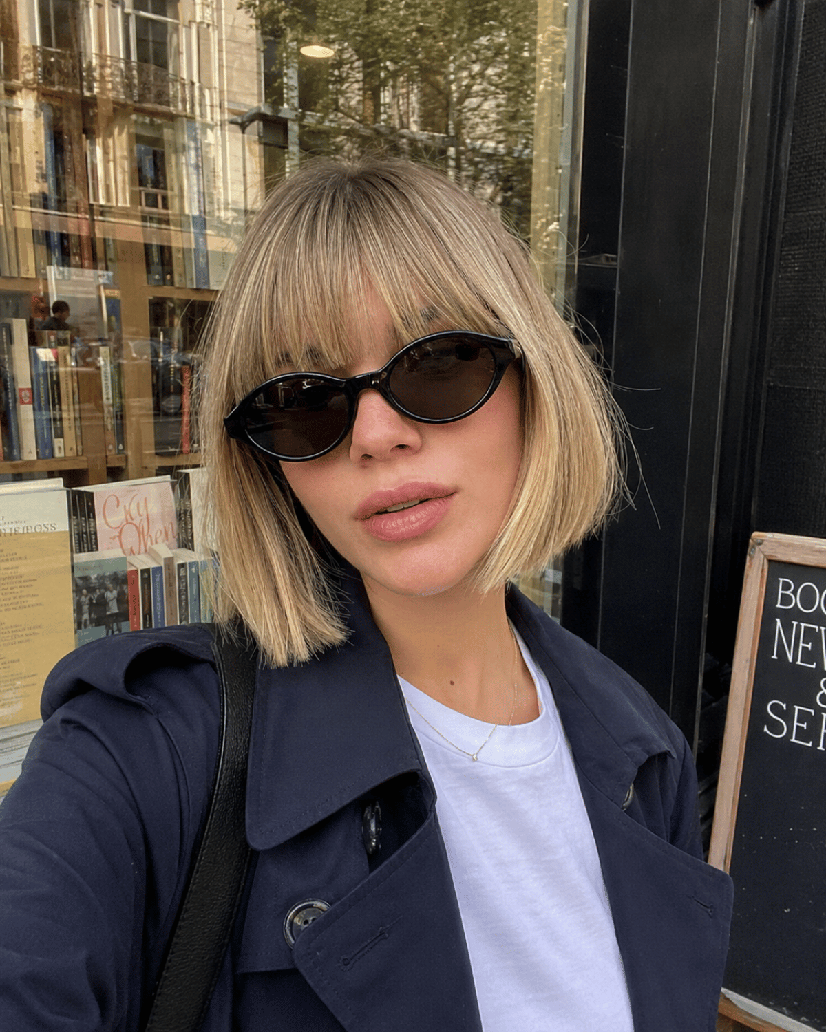Woman wearing a classic French bob haircut with full bangs, chin-length shape, and soft natural texture in an urban setting.