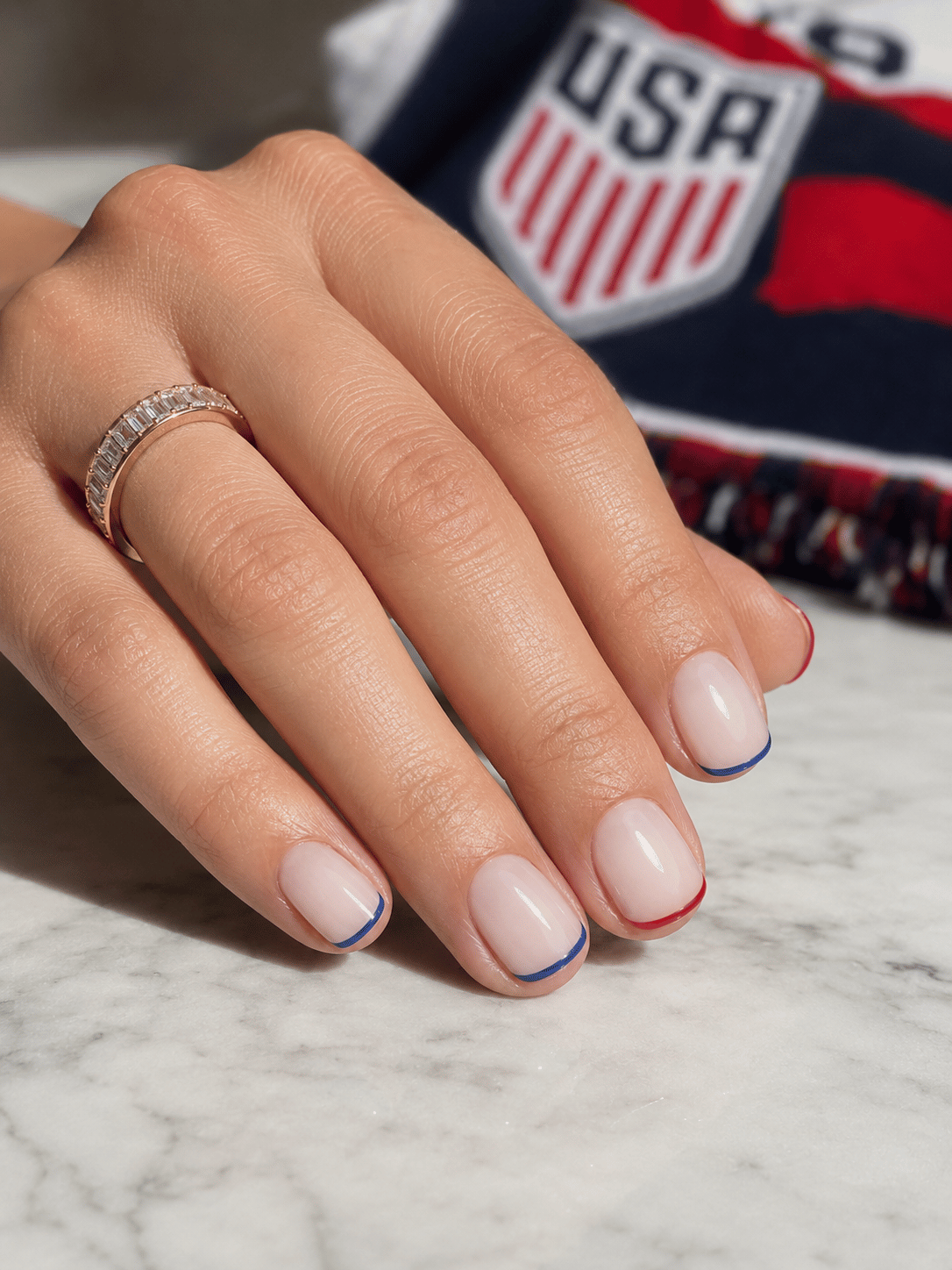 Minimal USA soccer nails with red and blue micro French tips on a sheer white base and short squoval nails