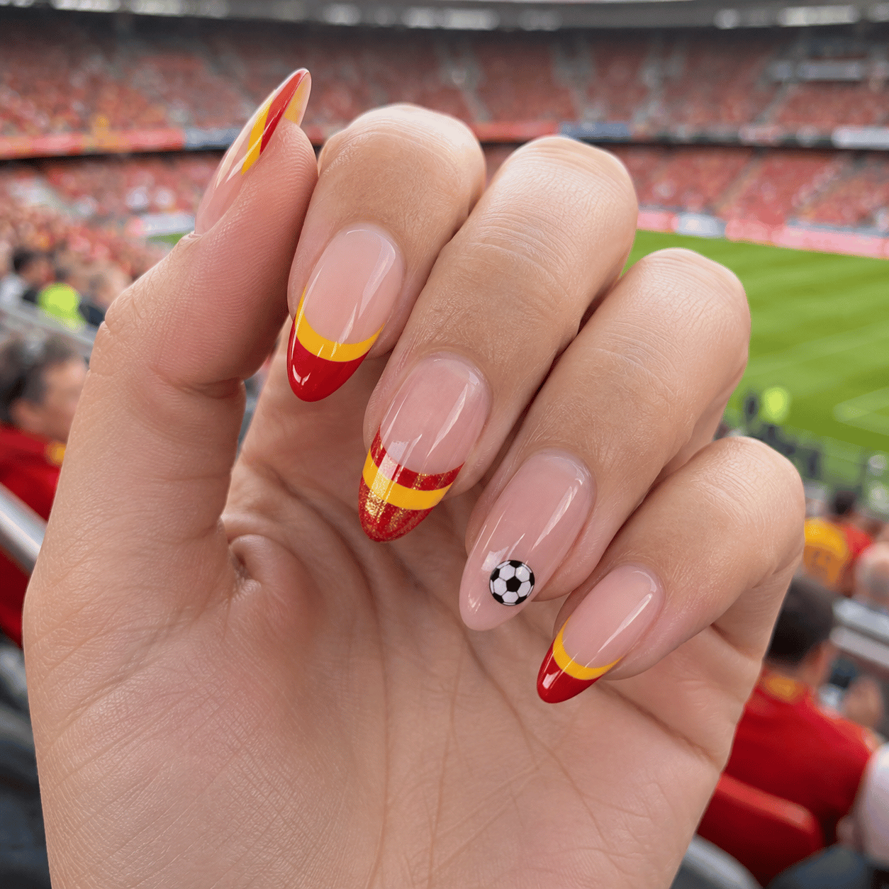 Spain football fan nails featuring red and yellow Spanish flag French tips on glossy almond nails at a football stadium.
