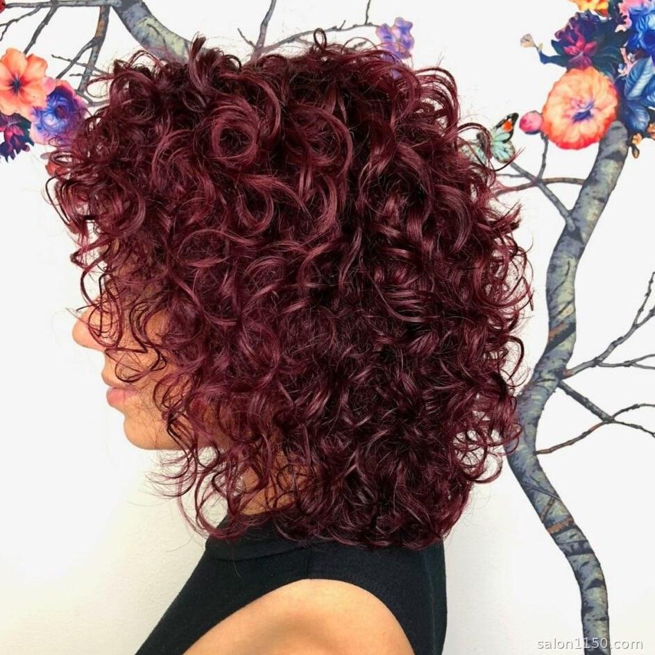 Wine-toned burgundy hair color on a woman with cool skin undertones and curly hair