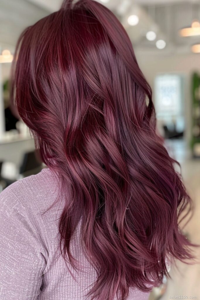 Woman with medium-length wavy burgundy hair color shown in natural salon lighting